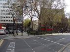 Cross to triangular garden with central fountain after crossing New Oxford Street