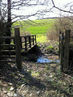 Bridleway through stream with a Footbridge to side.  At the end of Footbridge the Bridleway goes diagonally, to the left, uphill, across field to field
